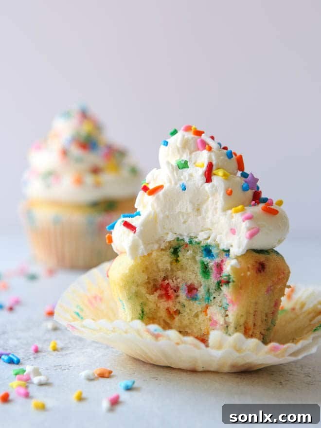 Two funfetti cupcakes, one bitten into to reveal its moist interior, with colorful sprinkles scattered around on a light background.
