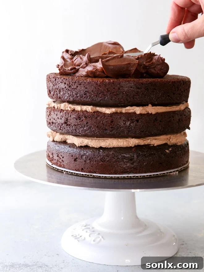 A chocolate sour cream cake being expertly frosted with an offset spatula