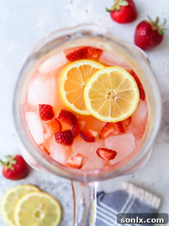 Freshly made easy strawberry lemonade in a pitcher with sliced lemons and whole strawberries, ready to be served on a hot summer day.