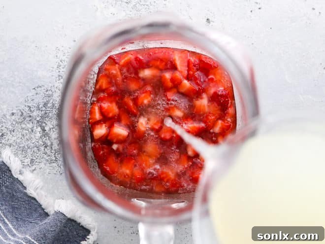 A large pitcher of freshly made strawberry lemonade being stirred, with ice and lemon slices, showing the vibrant red color.