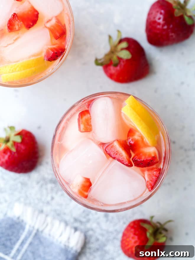 Close-up of a glass of strawberry lemonade, garnished with fresh lemon slices and a whole strawberry, on a white table.