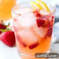 A glass of easy strawberry lemonade, garnished with fresh lemon and strawberry, next to a pitcher.