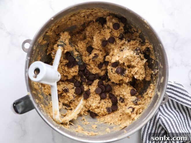 Close-up of chocolate chip oatmeal cookie dough mixing in a stand mixer bowl.