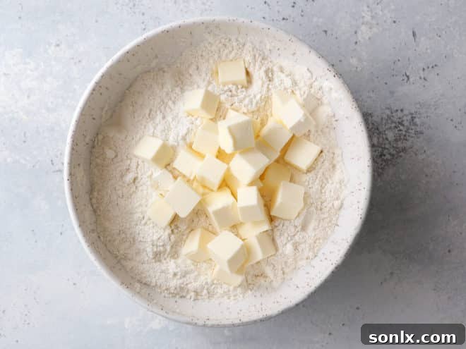 Cold butter cubes being tossed with dry ingredients in a mixing bowl.