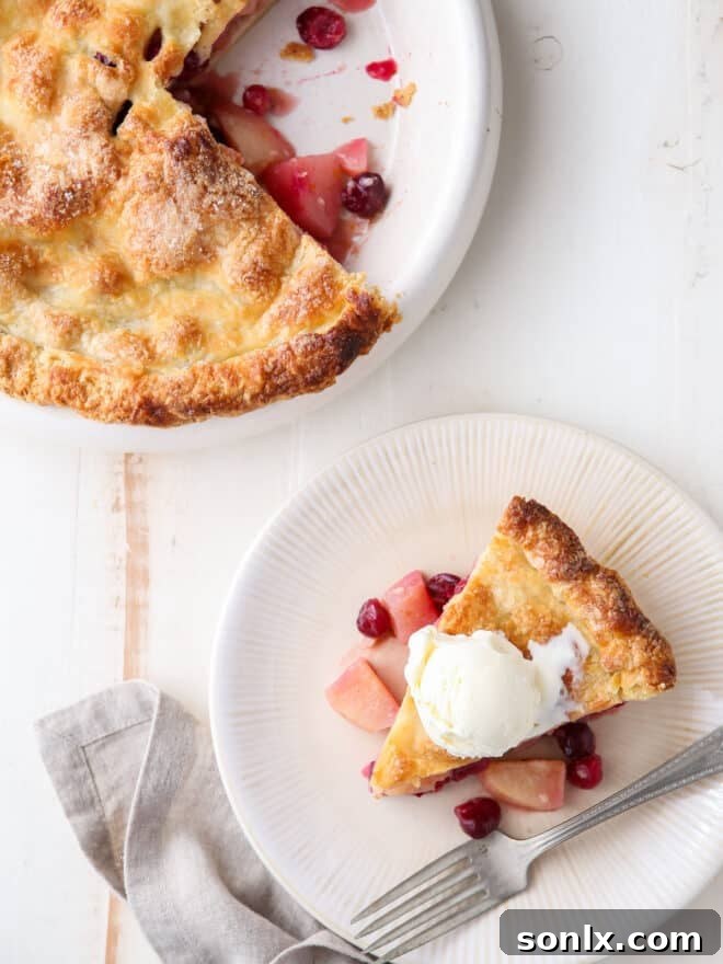 A whole cranberry pear pie with one slice removed, showcasing the golden-brown crust and a tantalizing glimpse of the fruit filling.