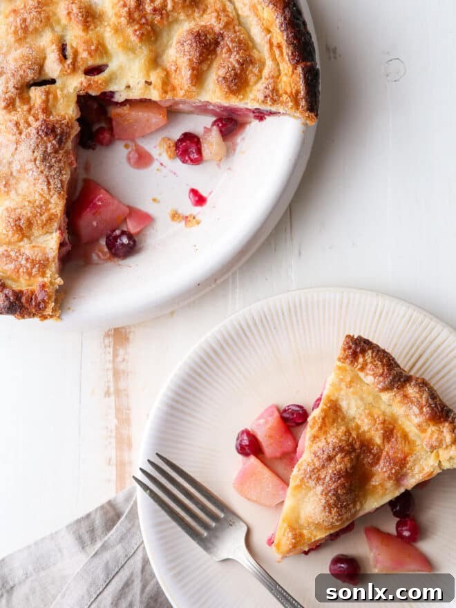 A beautifully baked cranberry pear pie with a slice on a plate, garnished with a fork and ready to be enjoyed.