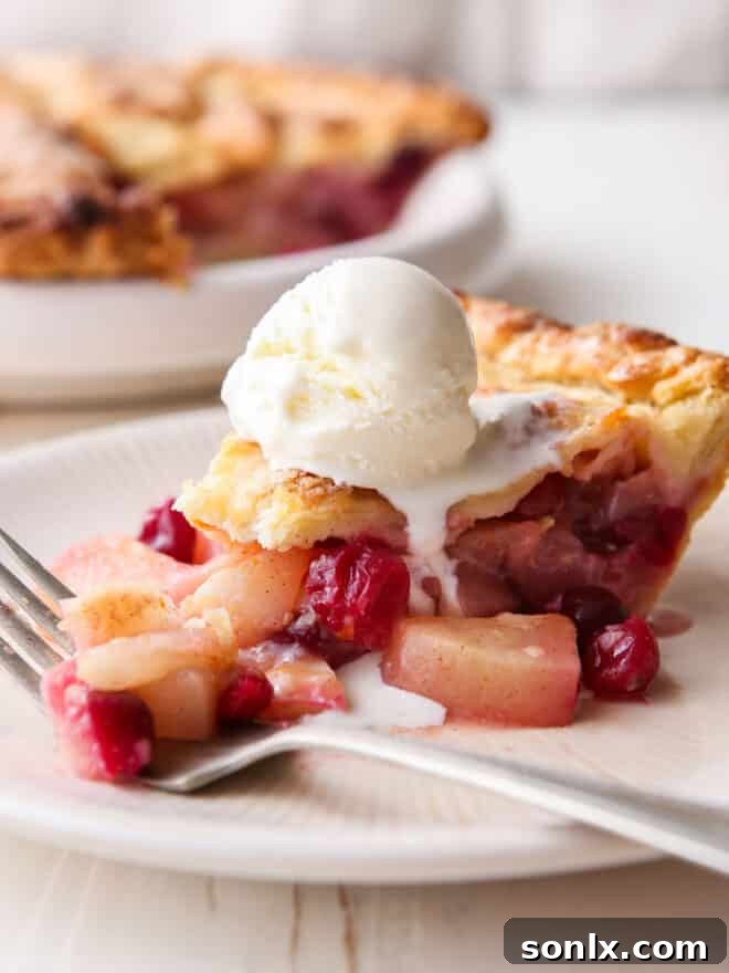 A close-up of a slice of cranberry pear pie on a plate with a fork and a scoop of vanilla ice cream, emphasizing the delicious texture.