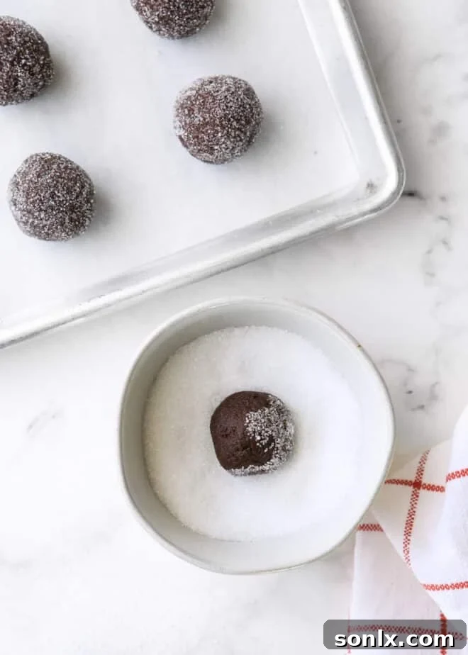 Cookie dough balls rolled in coarse sugar on a baking sheet, ready for indentations