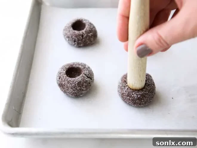 Thumbprint being gently pressed into a cookie dough ball using a wooden spoon handle