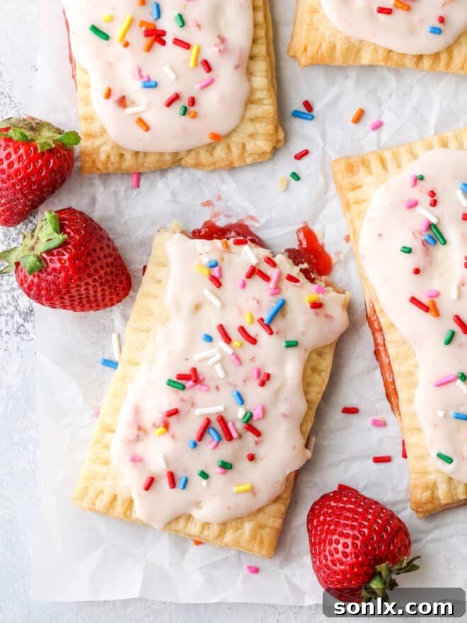 Artisan Strawberry Toaster Pastries 3 A close-up shot of a single homemade strawberry pop tart with pink frosting and rainbow sprinkles, showing the flaky crust and fruit filling.