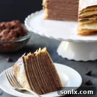 A slice of crepe cake with layers of crepes and whipped chocolate ganache, garnished with powdered sugar.