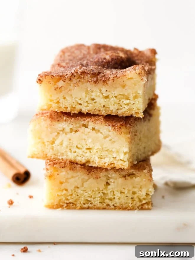 A perfectly stacked trio of warm cinnamon gooey butter bars, showcasing their inviting golden-brown tops and soft, rich layers.