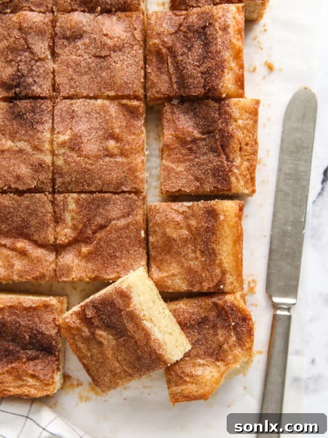 A close-up view of freshly baked cinnamon gooey butter bars, neatly sliced and arranged, with a knife resting alongside to emphasize their perfect texture.