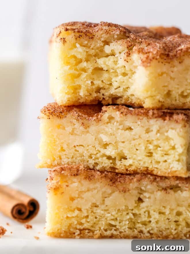 A tantalizing close-up of a stack of cinnamon gooey butter bars, with one bar showing a delicious bite taken out, revealing its soft, luscious interior.