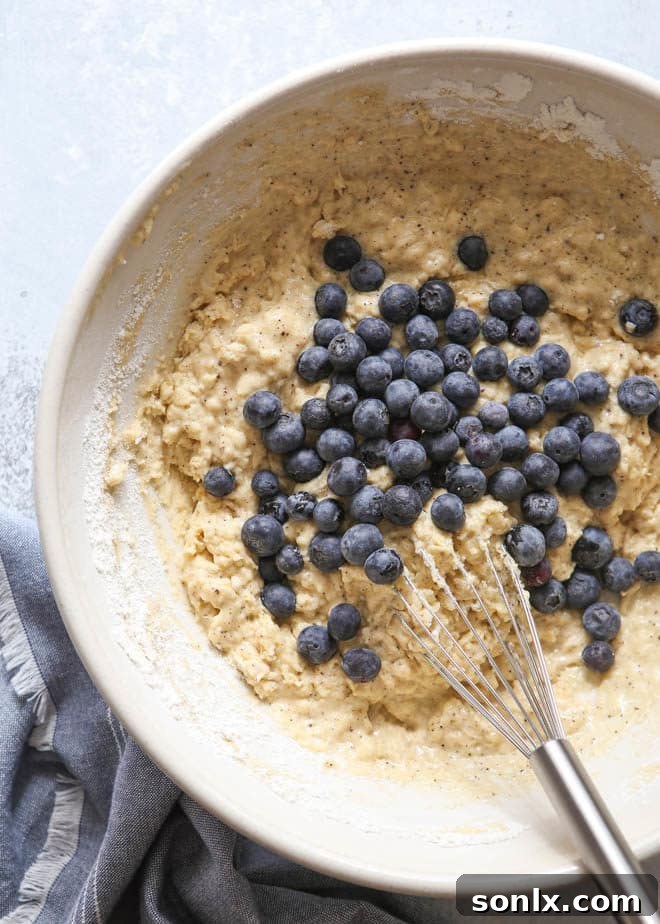 Detailed process shot showing a batch of blueberry muffins baking in a muffin tin, rising beautifully.