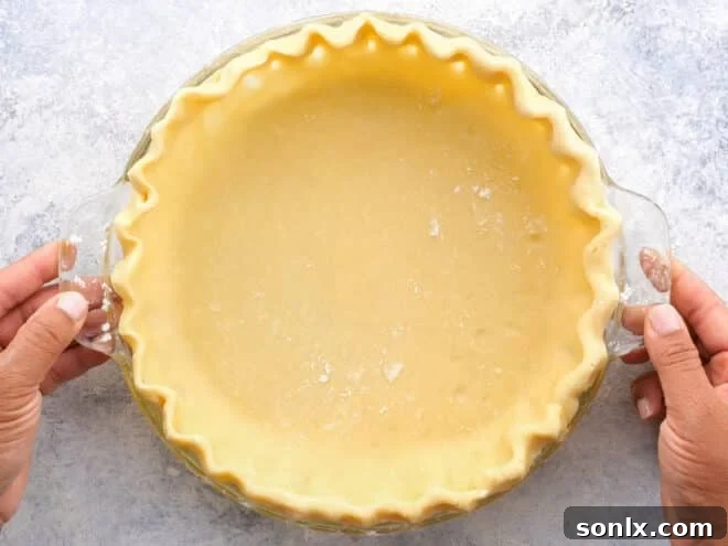 A meticulously prepared pie crust settled in a pie dish, ready for the next stage of blind baking.