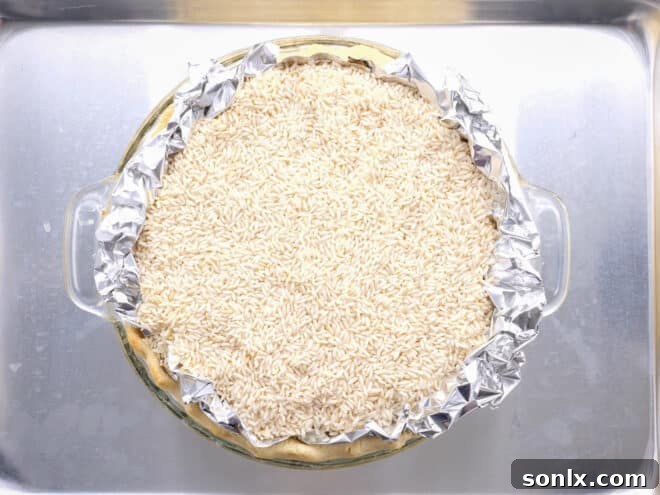 A pie crust partially blind baked, still filled with pie weights and lined with foil, demonstrating proper weight application.