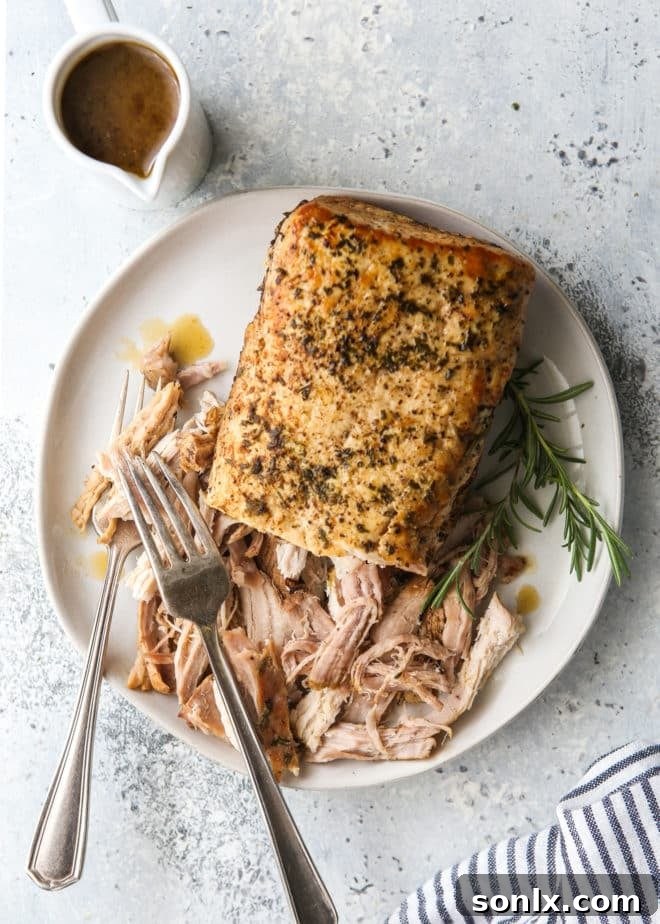 slow cooker rosemary balsamic pork roast shredded on a plate with gravy on the side
