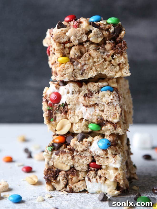 Close-up of freshly made Monster Marshmallow Cereal Treats, showcasing their gooey texture with visible chocolate chips, M&Ms, and oats on a cutting board.