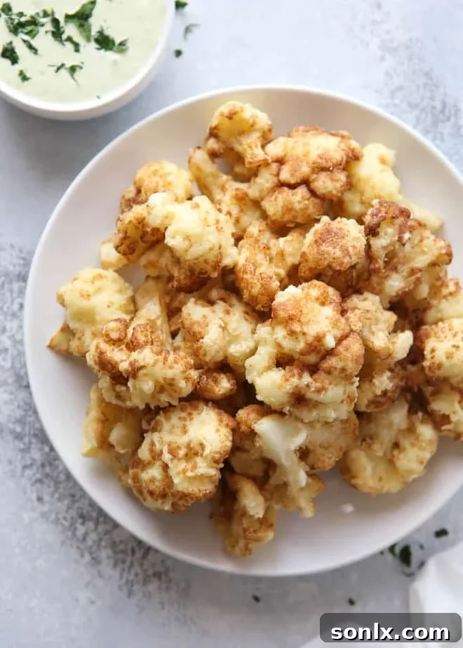 Golden-brown crispy tempura cauliflower florets, ready to be dipped, on a plate.