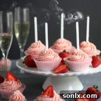 A beautifully decorated champagne cupcake topped with strawberry buttercream and a fresh strawberry slice