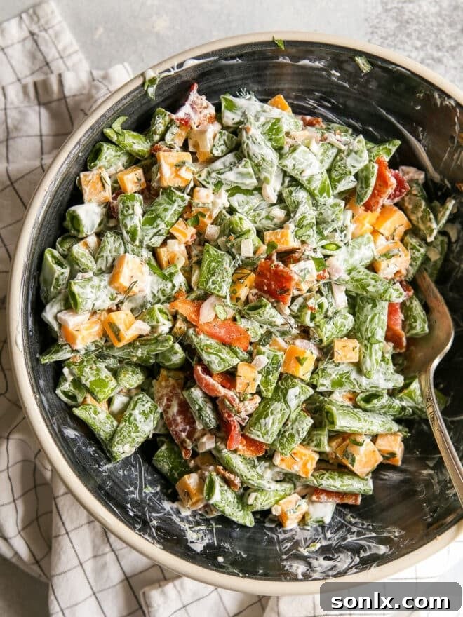 Mixing the creamy sugar snap pea salad with a spoon in a large bowl