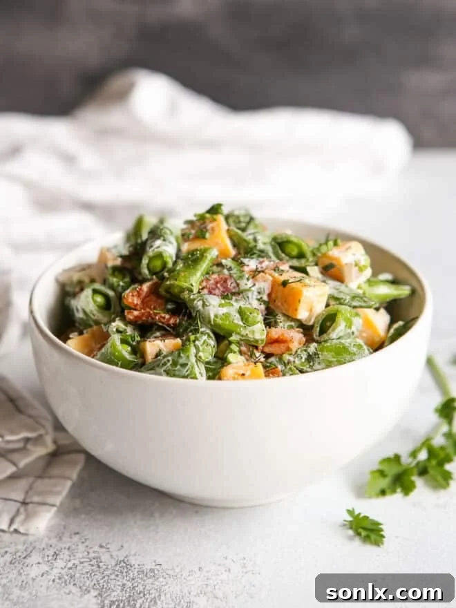 Close-up of creamy sugar snap pea salad with bacon and cheddar in a serving bowl, garnished with fresh herbs