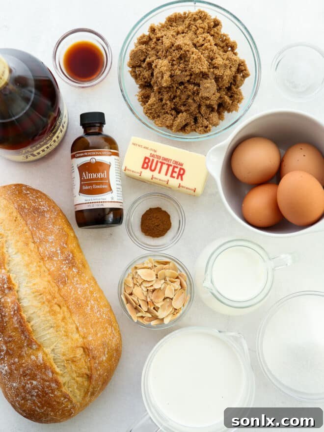 Measured ingredients for almond bread pudding laid out on a kitchen counter: bread cubes, whole milk, heavy cream, eggs, sugar, almond extract, and spices.