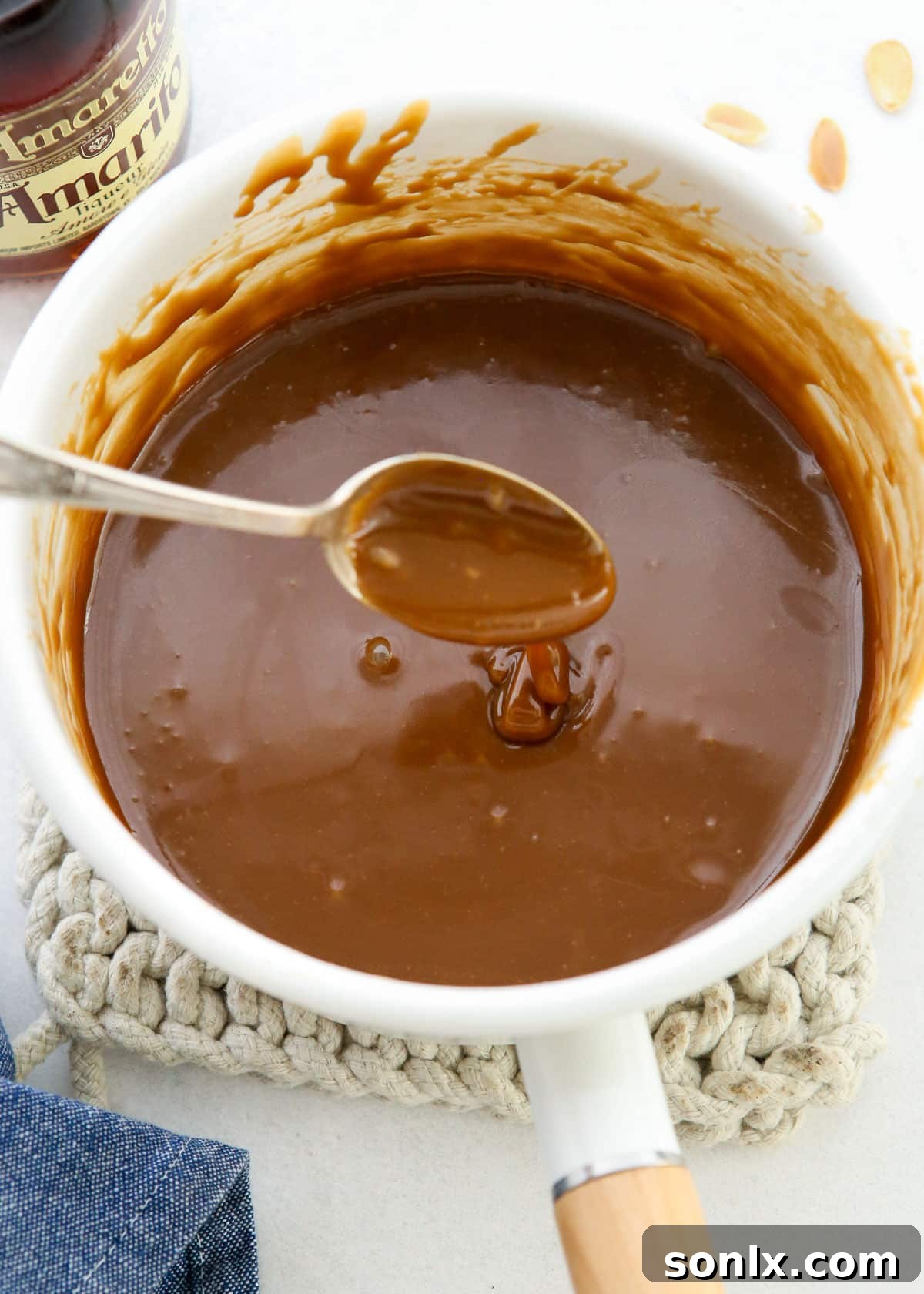 A small saucepan filled with a rich, bubbling homemade caramel amaretto sauce, simmering on a stovetop.