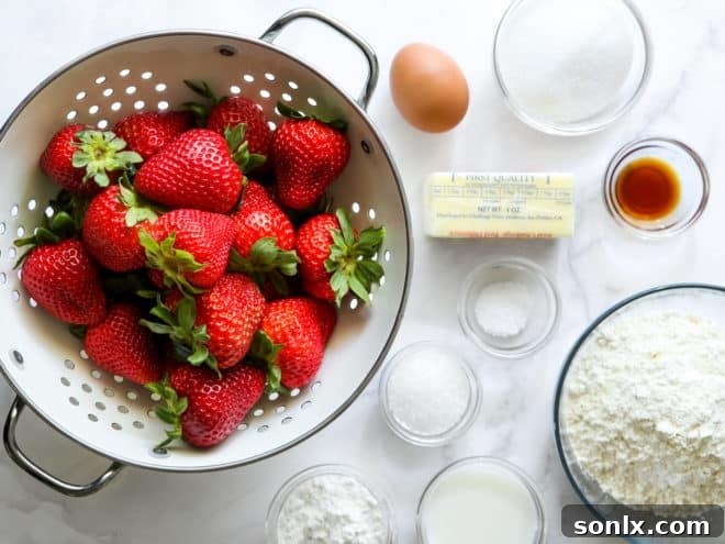 A flat lay photograph displaying all the fresh ingredients needed to bake a homemade strawberry skillet pie, including sliced strawberries, flour, sugar, and butter.