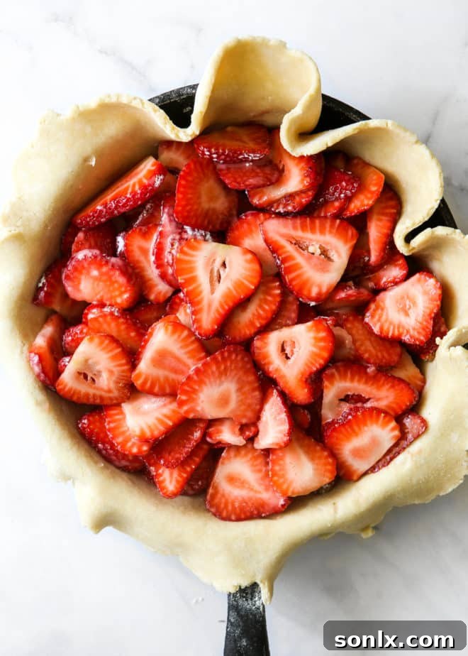 A cast iron skillet neatly lined with a single pie crust, brimming with a generous layer of glistening, sliced fresh strawberries, ready for baking.
