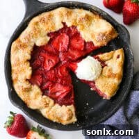 A vibrant slice of strawberry skillet pie adorned with a generous scoop of vanilla ice cream, showcasing its golden, flaky crust and bubbling fruit filling.