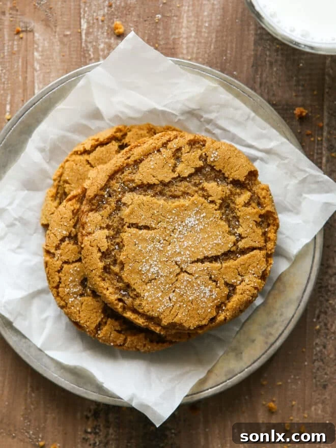 A beautifully arranged stack of golden-brown chewy gingersnap cookies on a white plate, accompanied by a refreshing glass of milk, highlighting their perfect texture and festive appeal.
