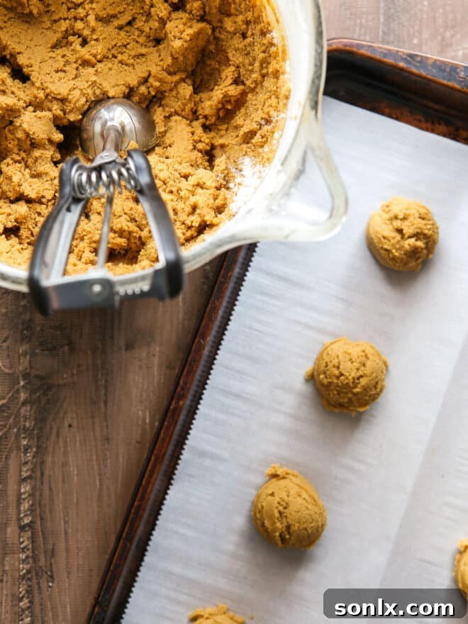 A cookie scoop forming uniform balls of dough, with several neatly arranged dough balls waiting on a baking sheet, ready for the oven.