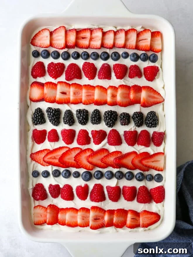 A slice of homemade berry poke cake revealing the layers of cake, berry filling, and whipped cream