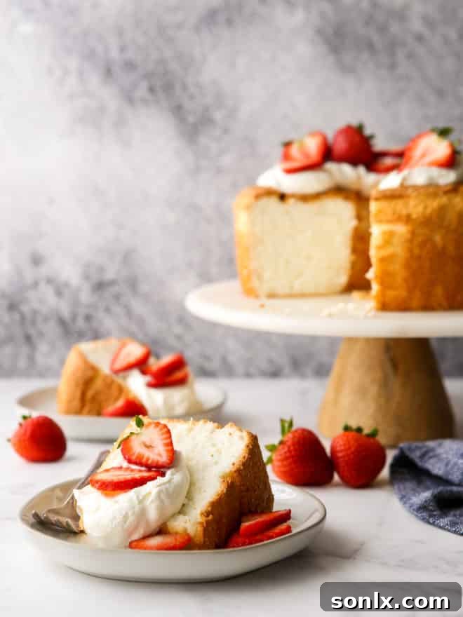 Sliced angel food cake with whipped cream and fresh strawberries on white plates, ready to be served.
