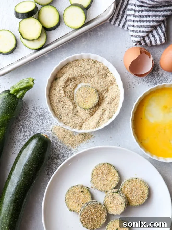 Close-up view of zucchini slices being dredged in breadcrumbs on a shallow plate, part of the breading process.