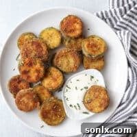 Close-up of golden-brown pan-fried zucchini chips on a plate, ready to be served as a delicious snack or appetizer.