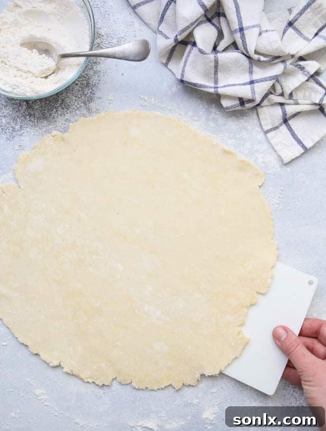 A rolling pin moving across a floured surface with pie dough, preventing sticking.