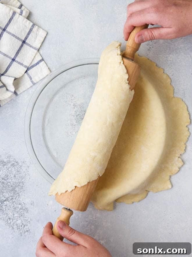 A person carefully rolling pie dough onto a rolling pin for easy transfer to a pie dish.