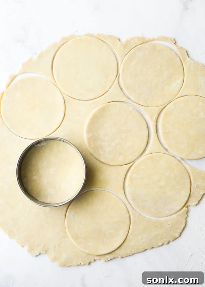 Close-up of hands using a round cutter to meticulously cut circles from a rolled-out sheet of pie dough for blueberry hand pies.