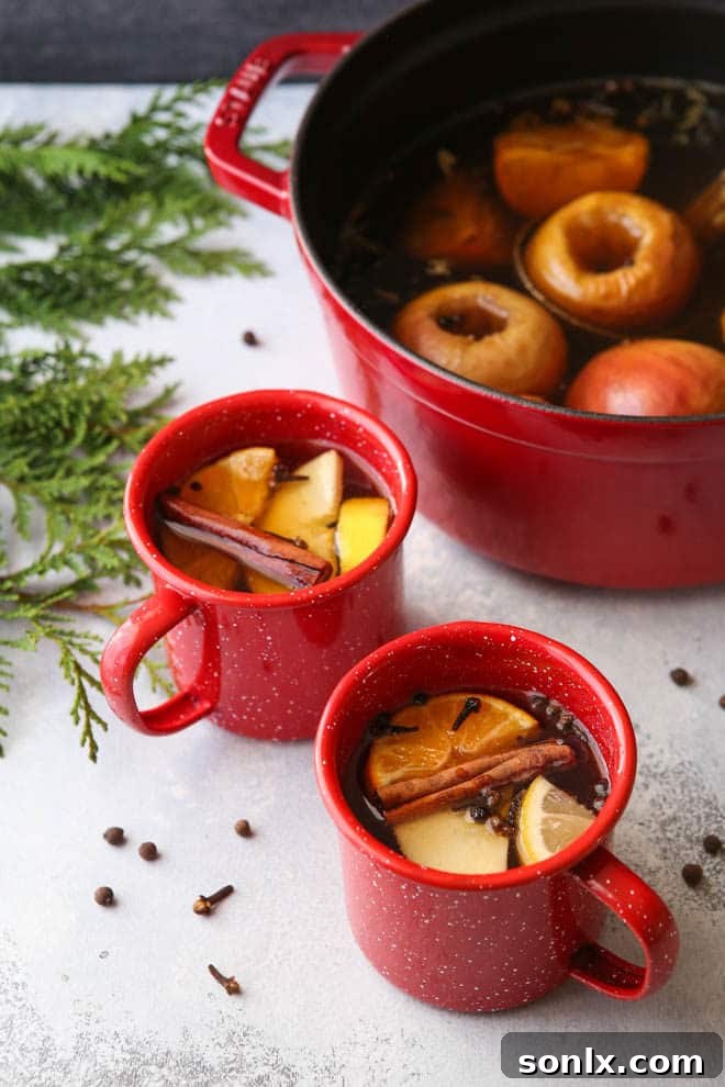 A close-up shot of a steaming mug of boozy hot wassail, garnished with orange slices and cinnamon, next to a festive candle.