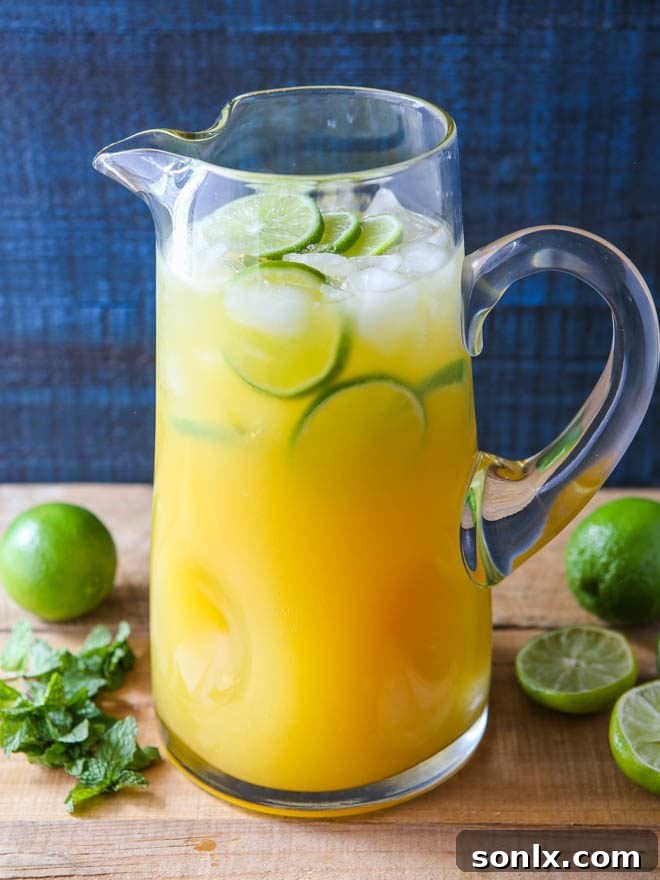 Close-up of a glass of Mango Pineapple Punch, showing the vibrant yellow liquid, ice cubes, and a fresh lime slice.