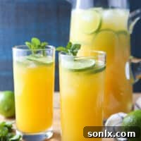 A vibrant pitcher of Mango Pineapple Punch, garnished with fresh lime slices and mint sprigs.