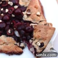 A slice of sweet cherry and hazelnut galette on a white plate with a fork.
