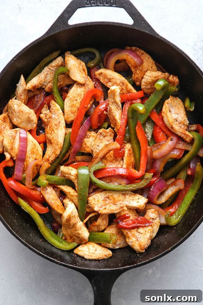 Sizzling chicken fajita mixture with colorful bell peppers and onions in a cast iron skillet.