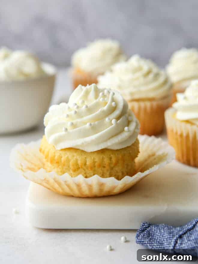 An array of delicious vanilla cupcakes, some frosted, others plain, on a rustic wooden surface.
