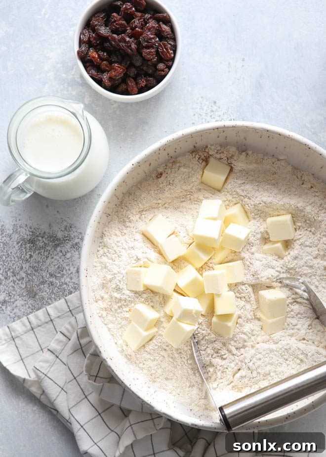 A baker's hands mixing dough for hot cross biscuits in a bowl, showing the initial stages of preparation and texture
