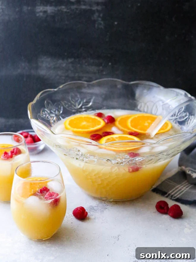 Large punch bowl filled with sparkling mimosa punch, garnished with orange slices and fresh raspberries, ready for a brunch party.