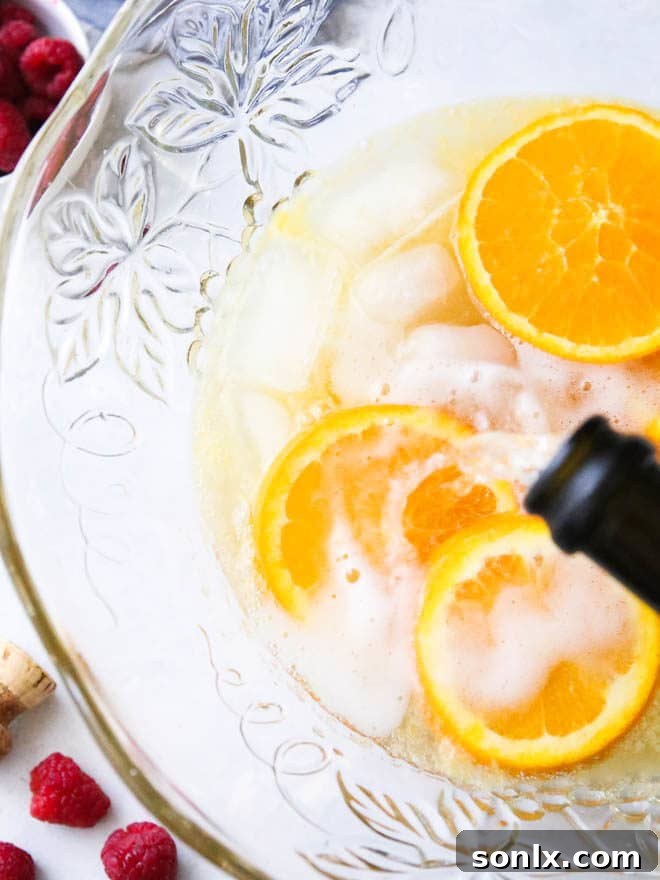 Close-up of a punch bowl brimming with Mimosa Punch, garnished with fresh orange slices and vibrant raspberries, inviting guests to serve themselves.